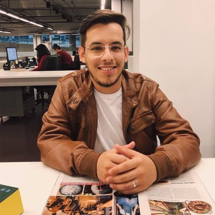 Um homem com uma jaqueta marrom está sentado em uma mesa com uma revista