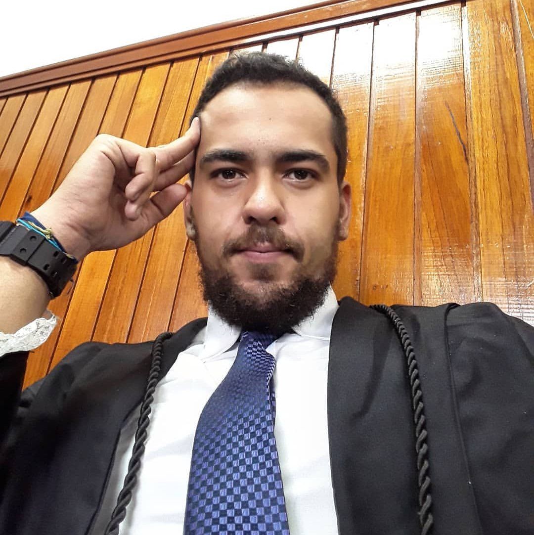 Um homem de terno e gravata está sentado em frente a uma parede de madeira.