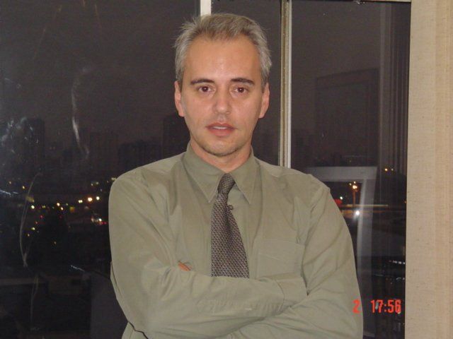 Um homem de camisa verde e gravata está com os braços cruzados