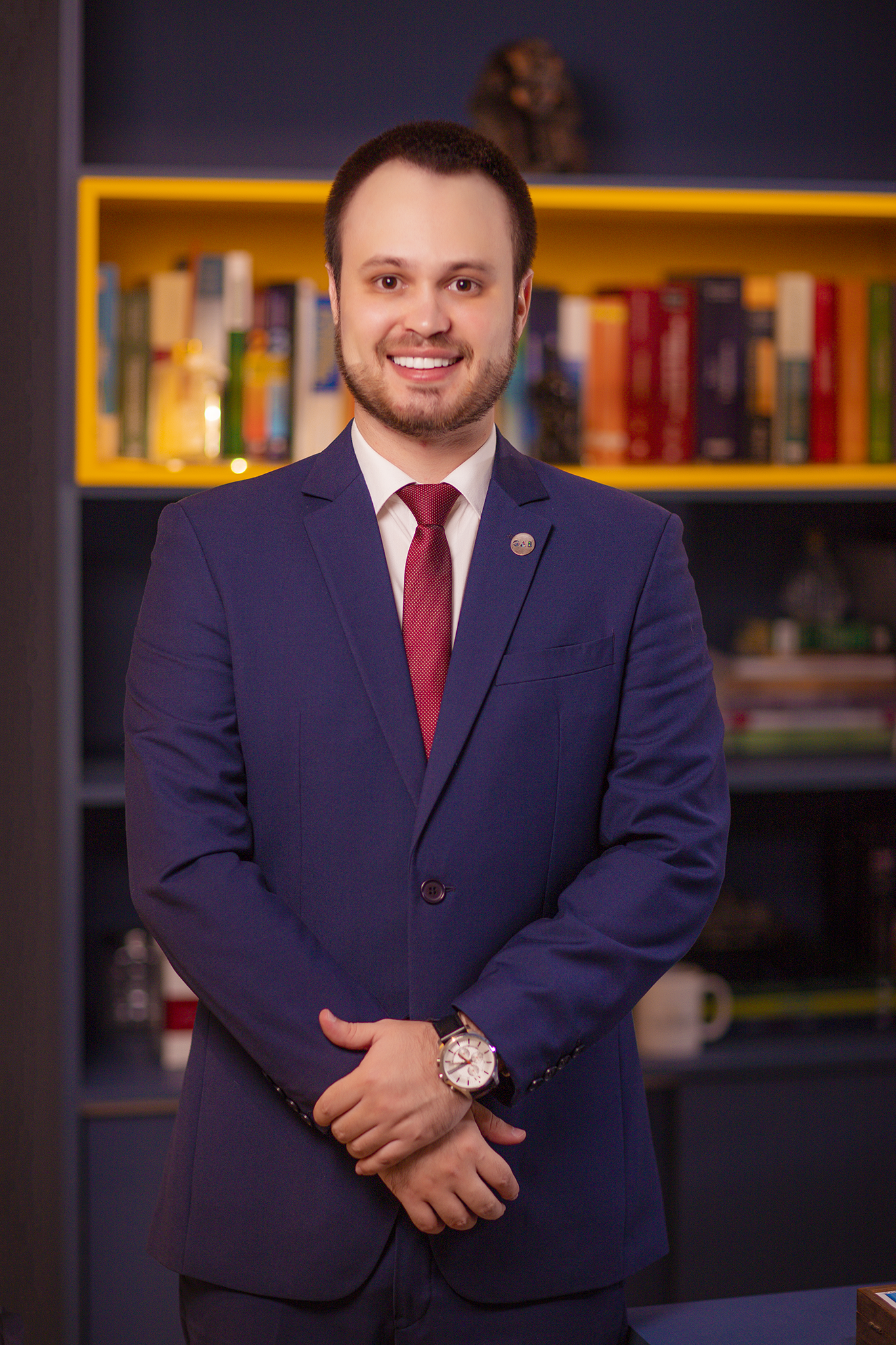 Um homem de terno e gravata está parado em frente a uma estante de livros.