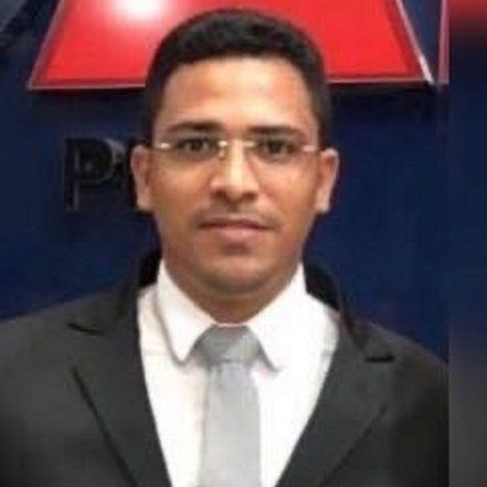 Um homem de terno e gravata está parado em frente a uma placa.