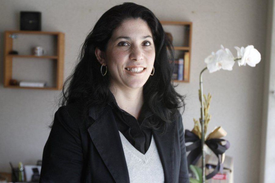Uma mulher de jaqueta preta está sorrindo na frente de uma orquídea