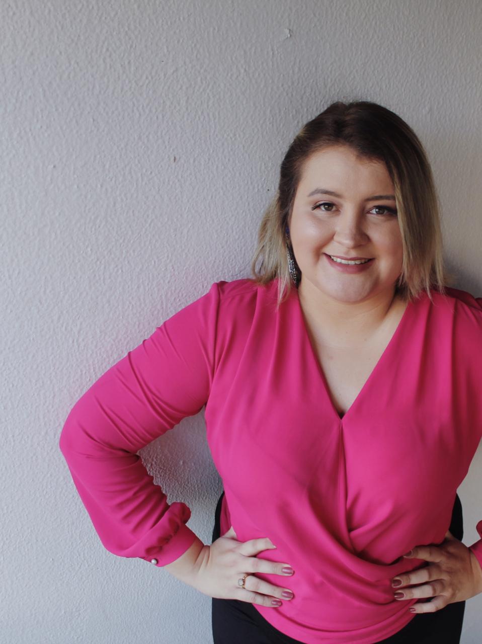 Uma mulher com uma blusa rosa está de pé com as mãos nos quadris