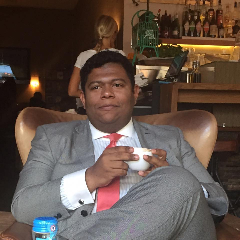 Um homem de terno e gravata está sentado em uma cadeira segurando uma xícara de café