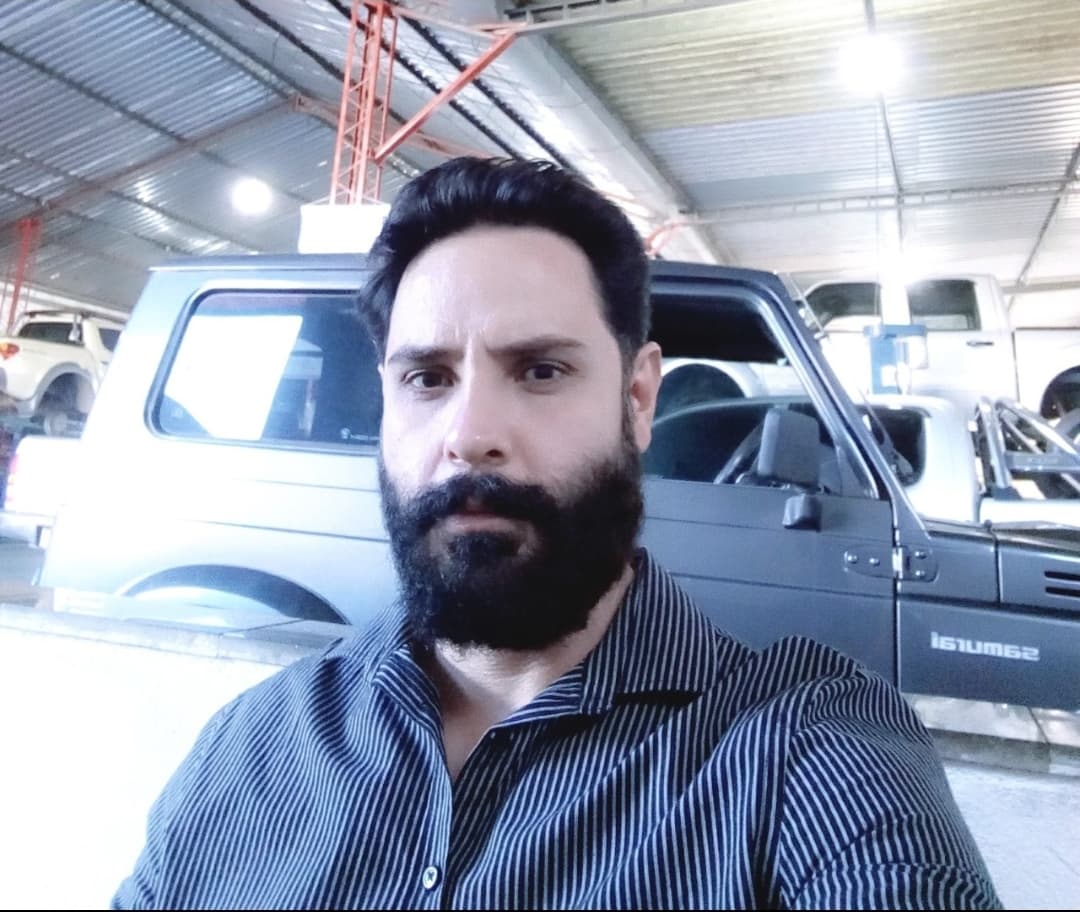 Um homem com barba está parado na frente de um carro