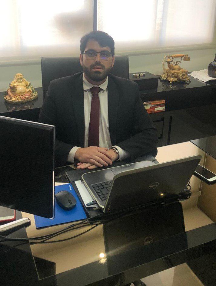 Um homem de terno e gravata está sentado em uma mesa com um laptop.