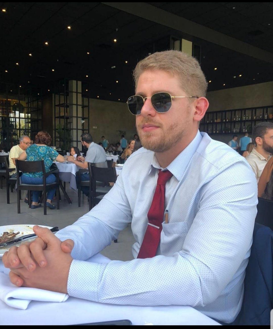 Um homem de óculos escuros e gravata vermelha está sentado à mesa