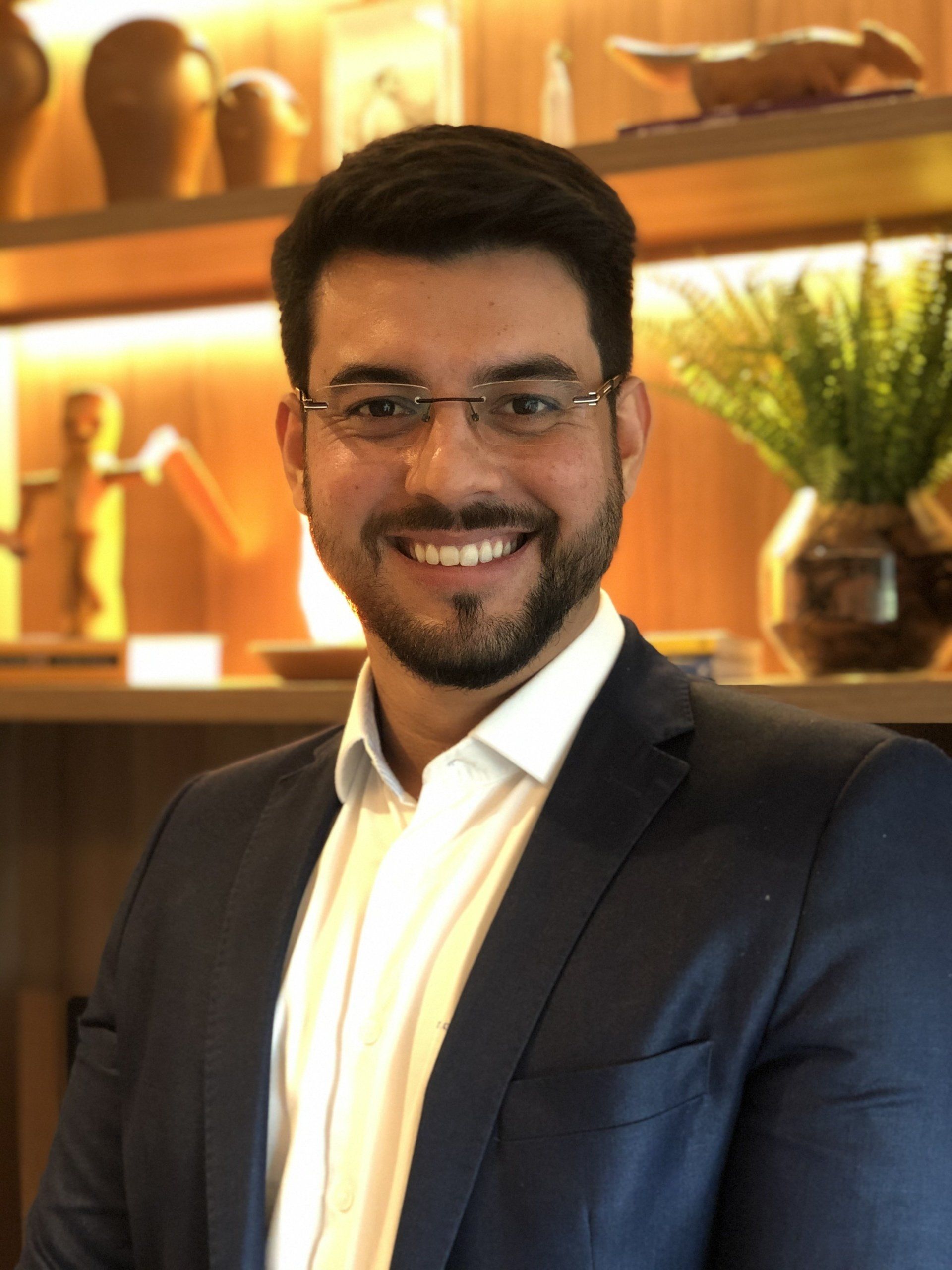 Um homem com barba, óculos e terno está sorrindo para a câmera.