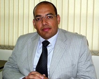 Um homem de terno e gravata está sentado em frente a uma janela.