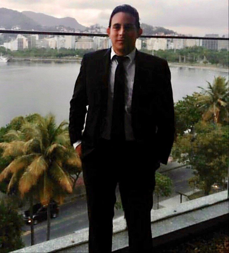 Um homem de terno e gravata está em uma varanda com vista para um corpo de água