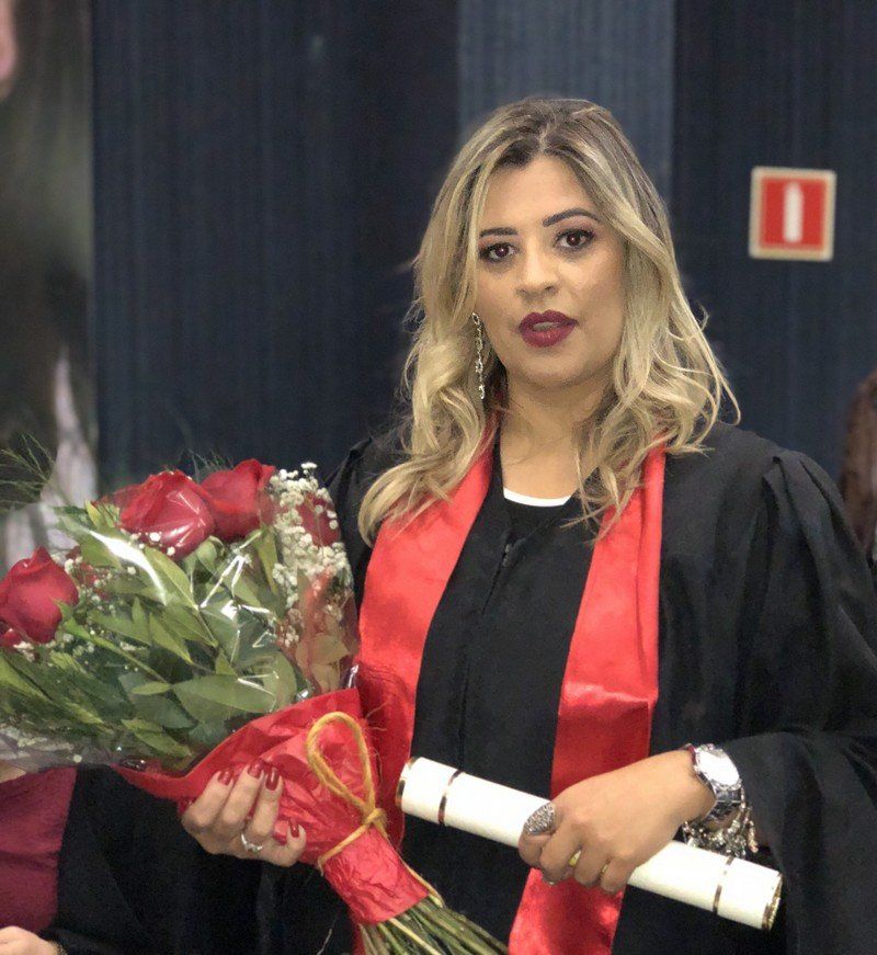 Uma mulher em um vestido de formatura está segurando um buquê de flores e um diploma