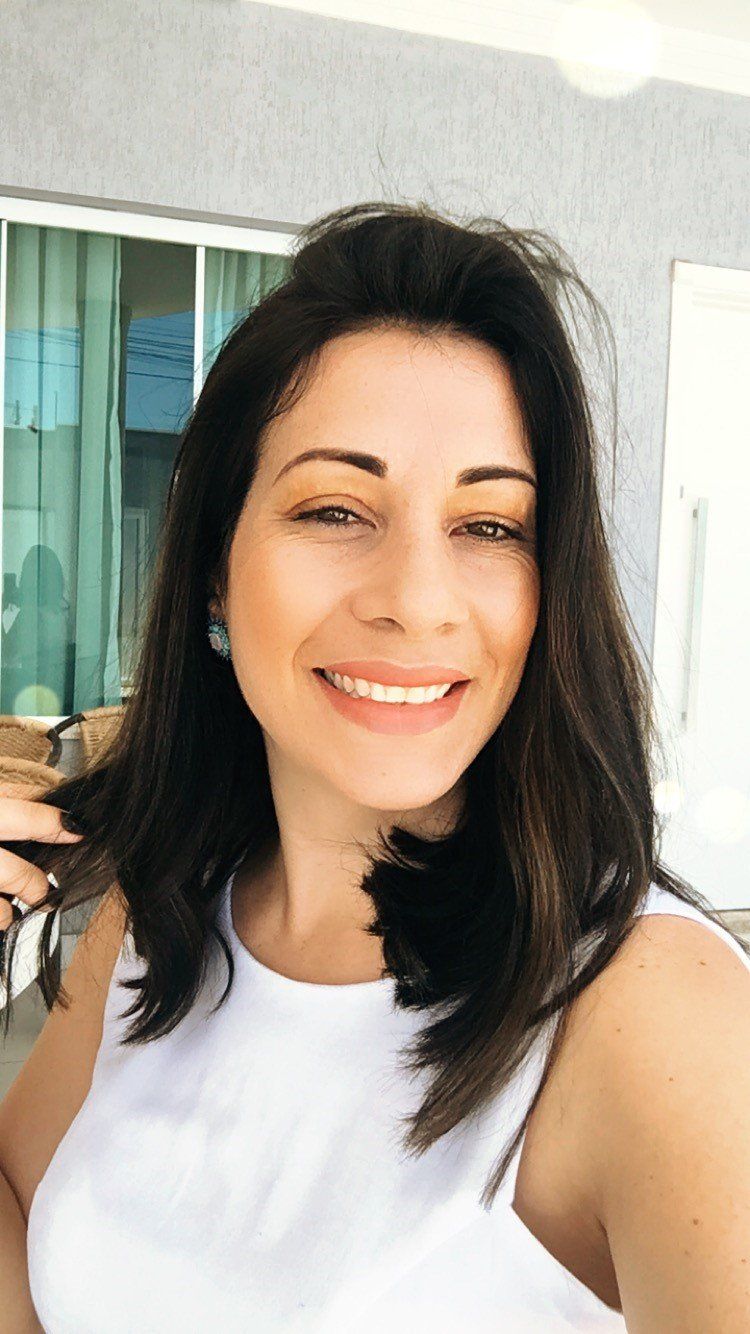 Uma mulher de blusa branca está sorrindo e segurando o cabelo.