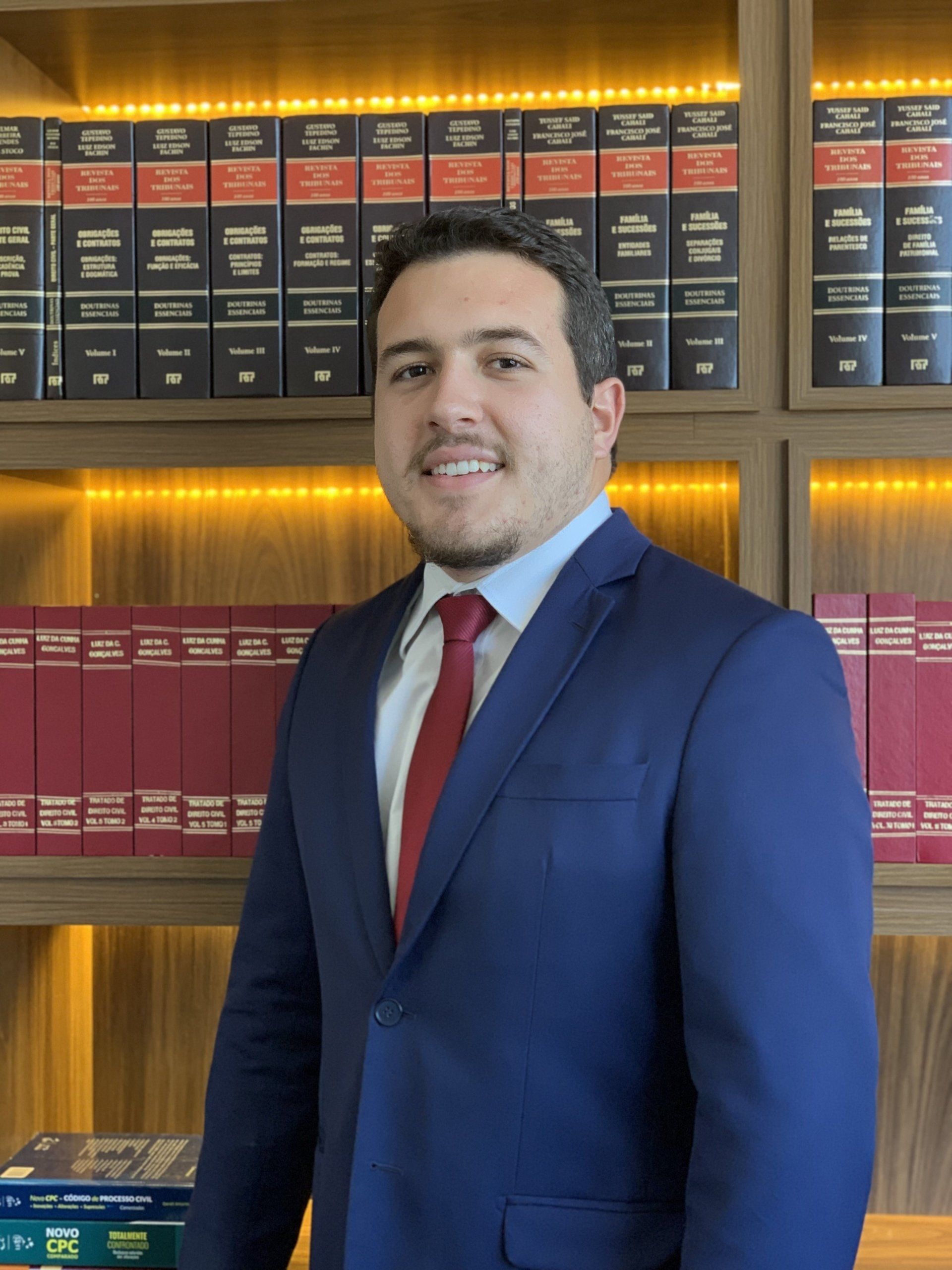 Um homem de terno e gravata está parado em frente a uma estante de livros.