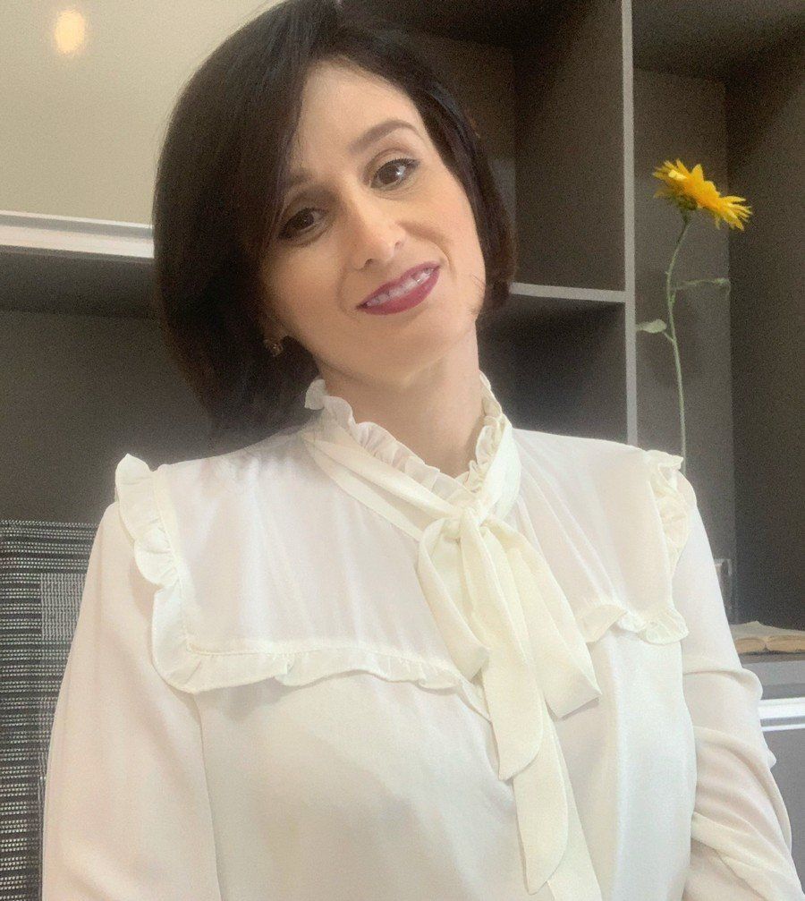 Uma mulher de camisa branca e gravata borboleta está em frente a um vaso de flores.