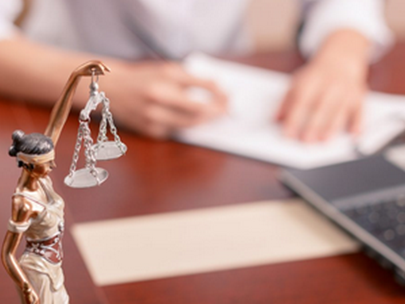 Uma estátua da senhora justiça está sentada em uma mesa ao lado de um laptop.
