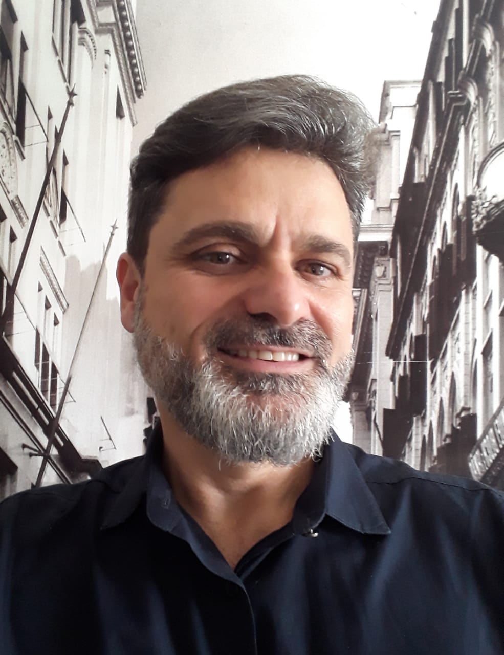 Um homem com barba está sorrindo na frente de um prédio