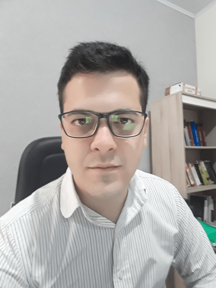 Um homem de óculos está sentado em uma cadeira em frente a uma estante.