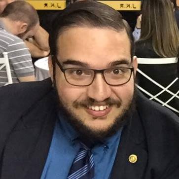 Um homem com barba e óculos está vestindo terno e gravata.