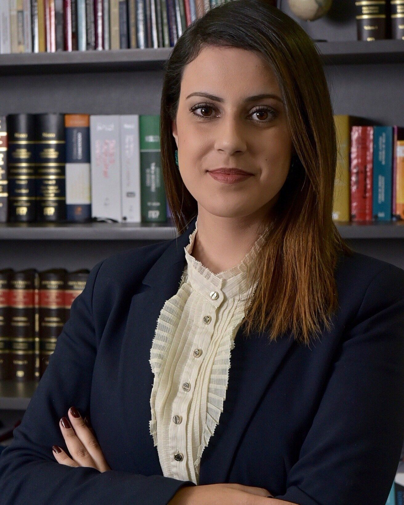 Uma mulher está parada em frente a uma estante com os braços cruzados.