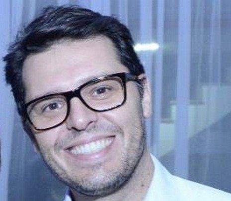 Um close de um homem usando óculos e sorrindo.