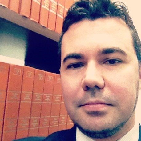 Um homem de terno e gravata fica em frente a uma estante de livros