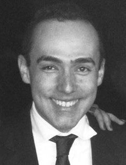 Um homem de terno e gravata está sorrindo em uma foto em preto e branco.