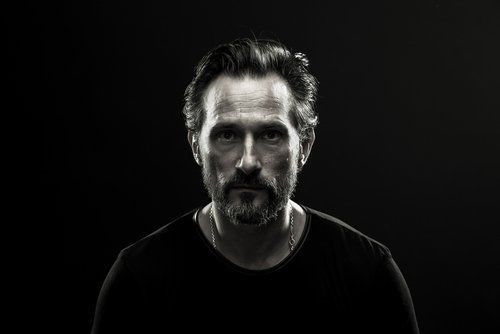 Um homem com barba está olhando para a câmera em uma foto em preto e branco.