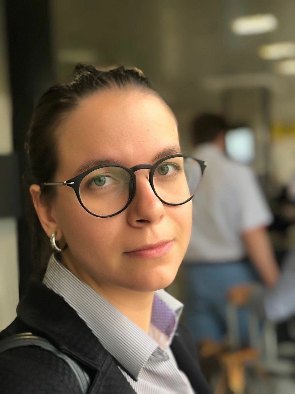 Uma mulher usando óculos e brincos está olhando para a câmera.