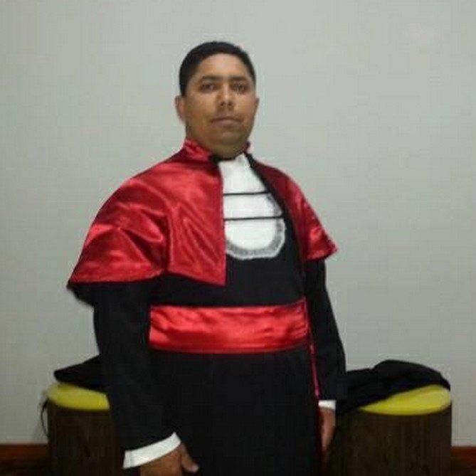 Um homem com um vestido de formatura está parado ao lado de um banquinho amarelo.