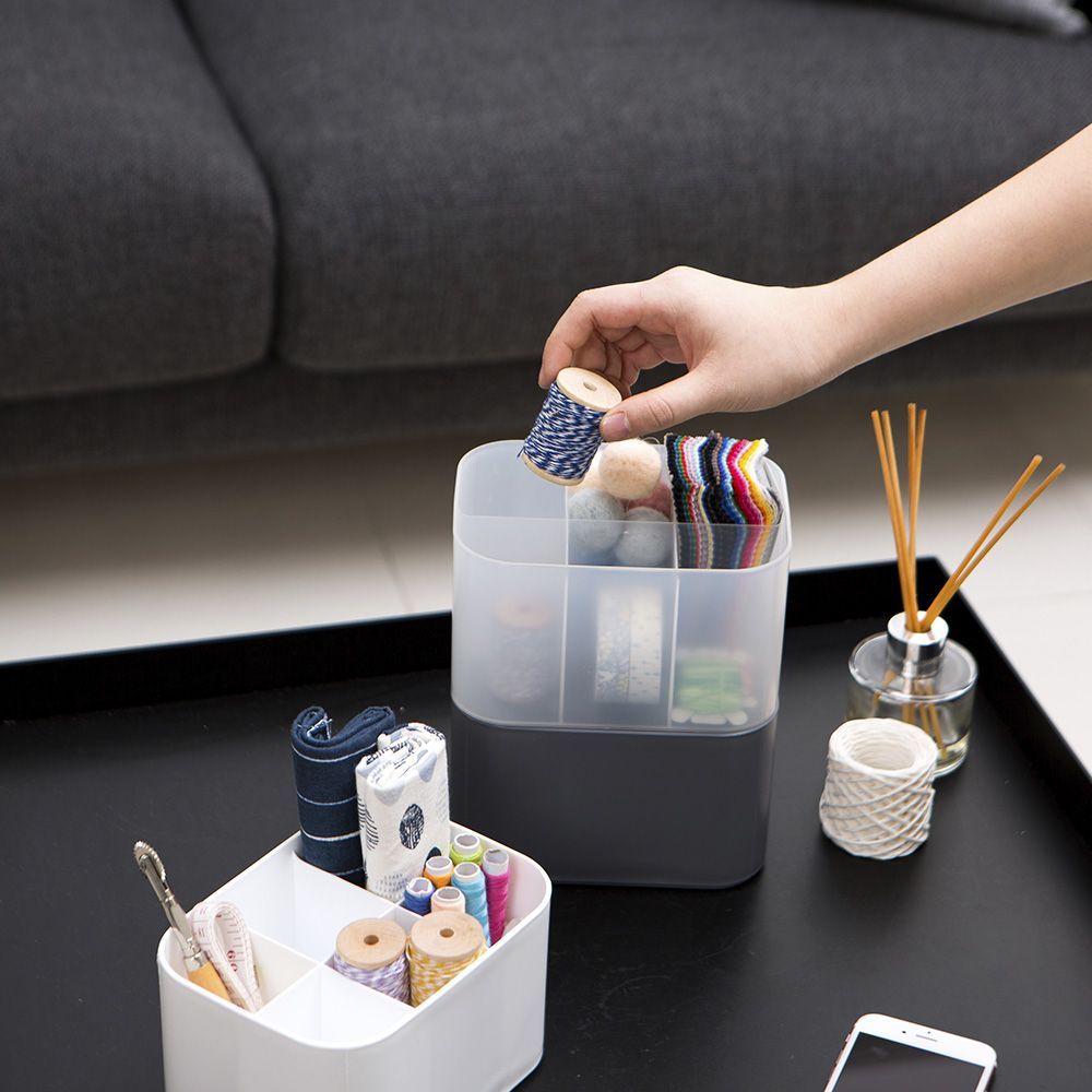 Una persona sostiene un carrete de hilo en un recipiente transparente sobre una mesa.