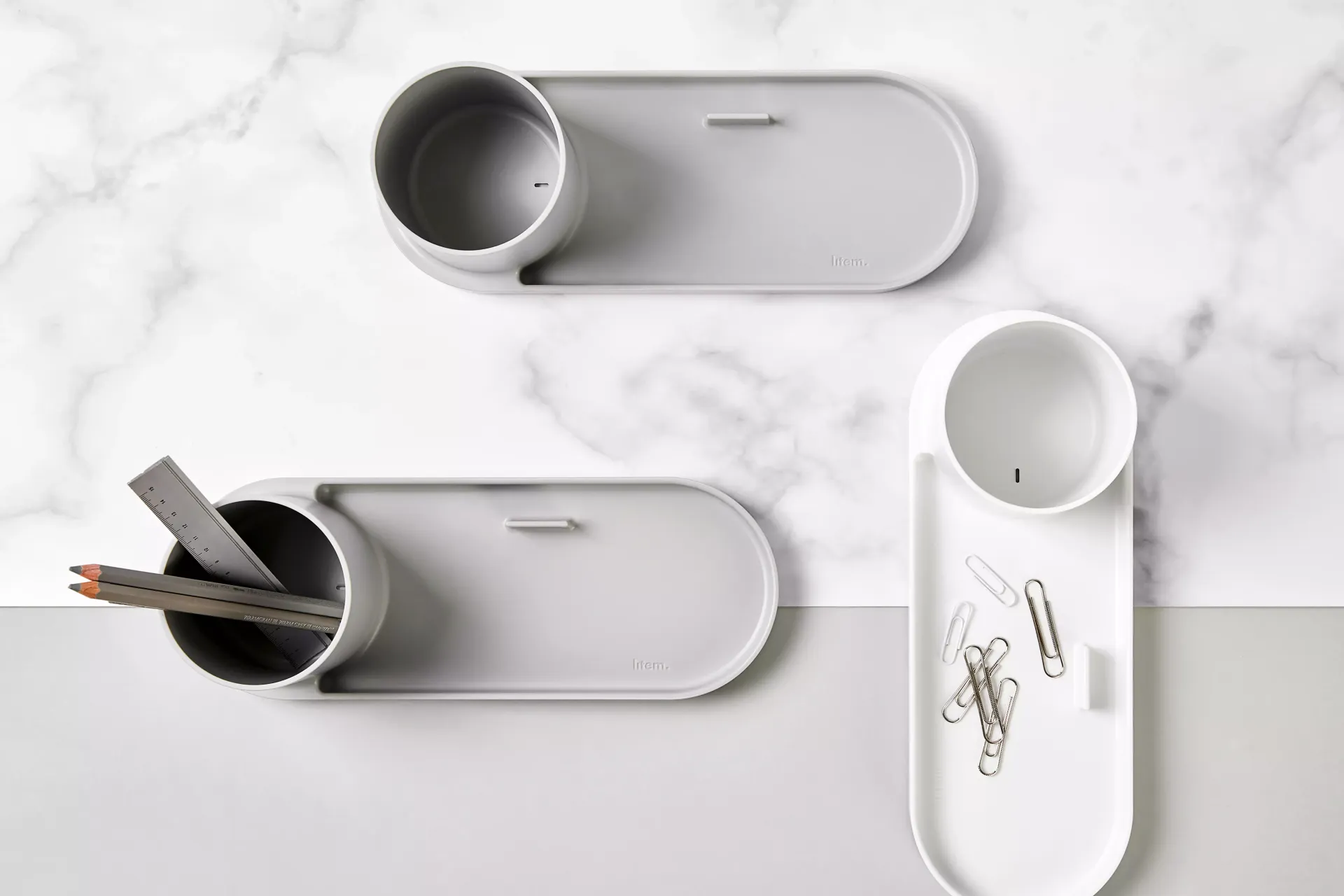 Hay tres bandejas con lápices y clips sobre una mesa.