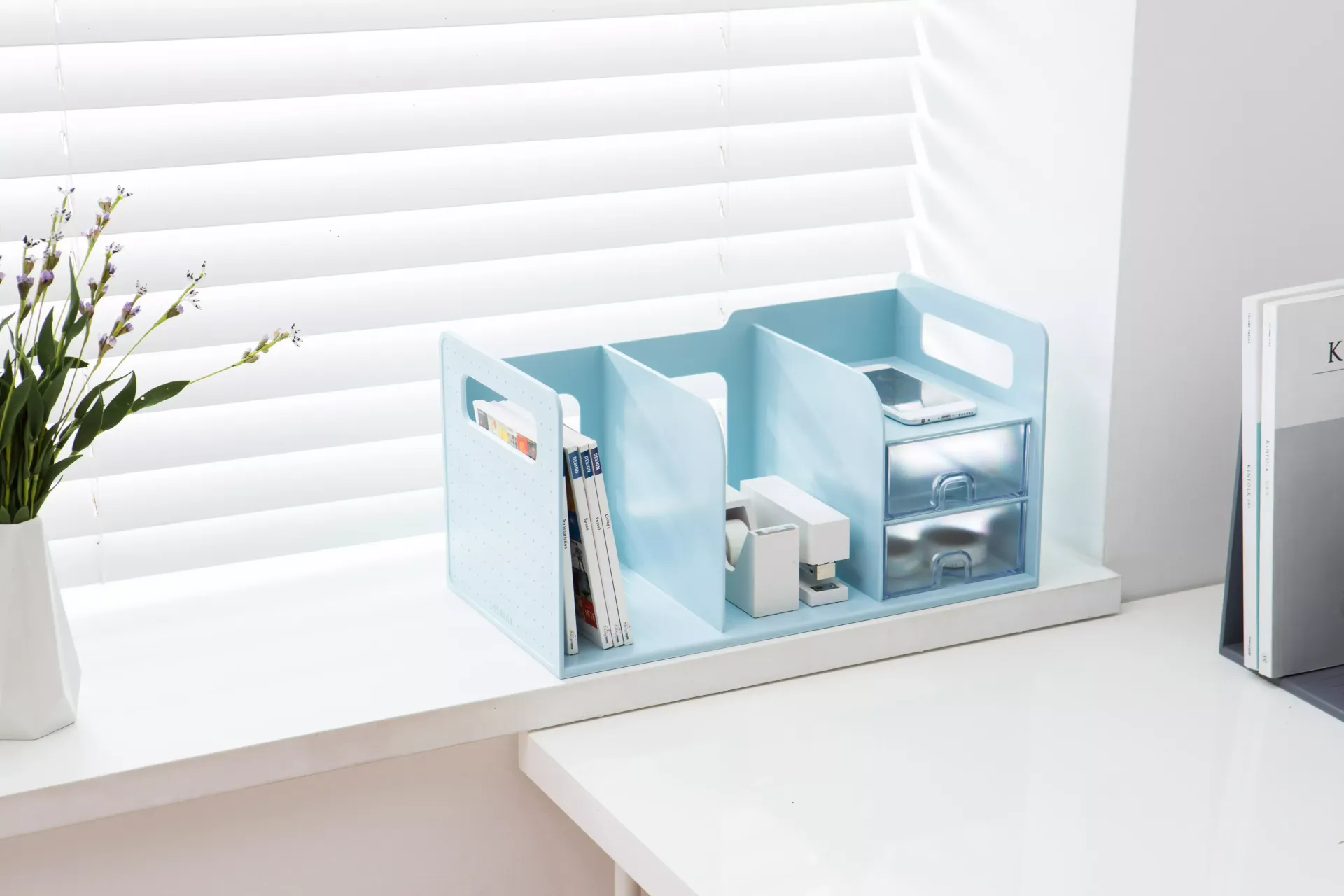 Una estantería azul está sobre una mesa blanca junto a una ventana.