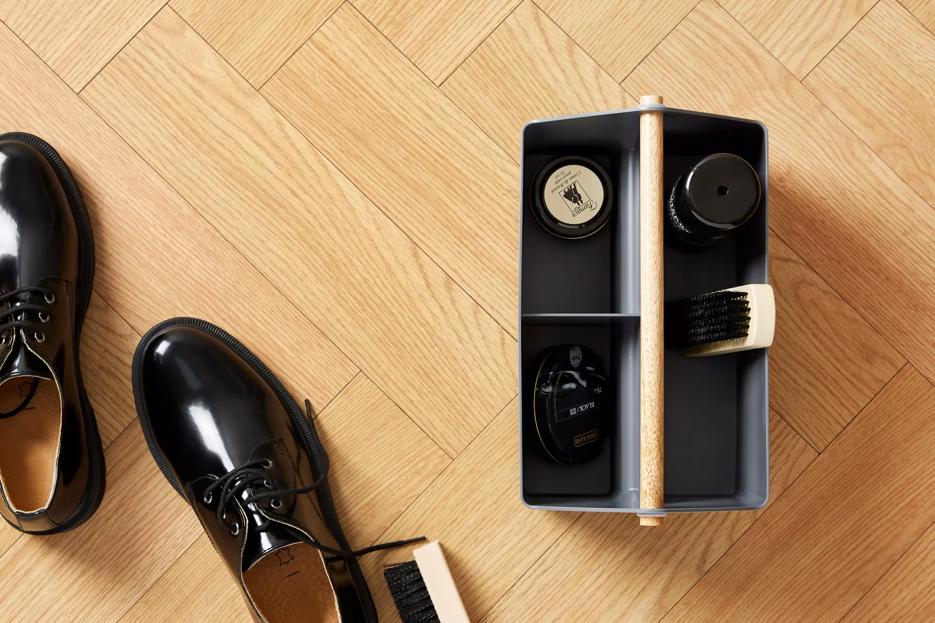 Un par de zapatos negros y una engrasadora sobre un suelo de madera.