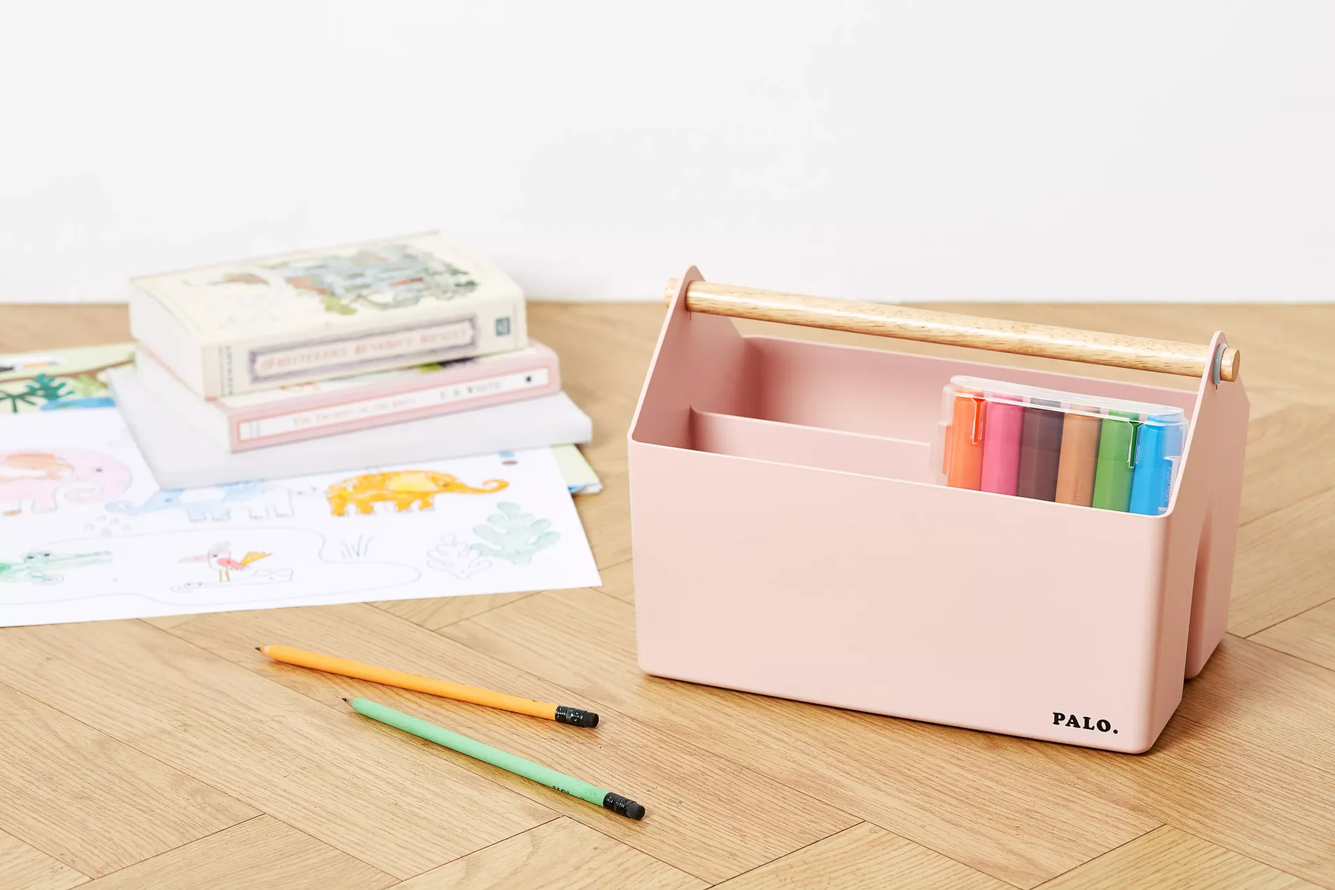 Una caja rosa con un asa de madera está sobre una mesa de madera junto a una pila de libros.