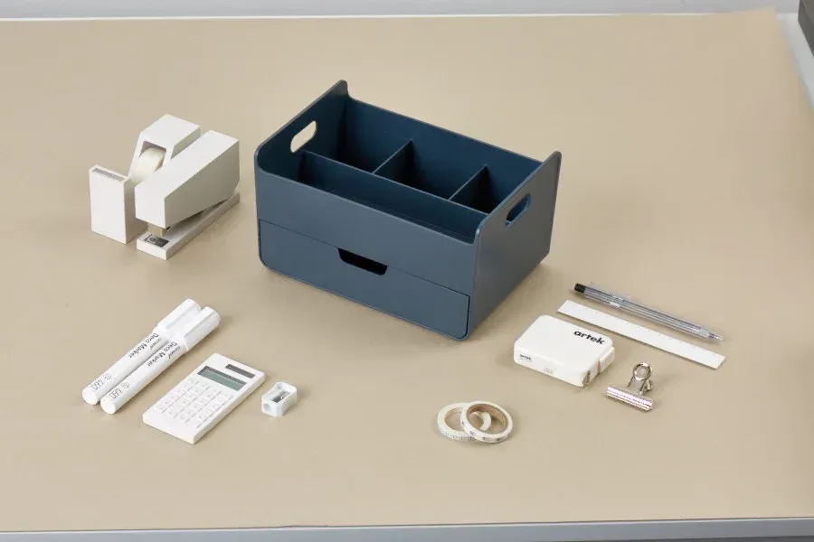 Uma mesa com uma caixa e um monte de material de escritório em cima dela