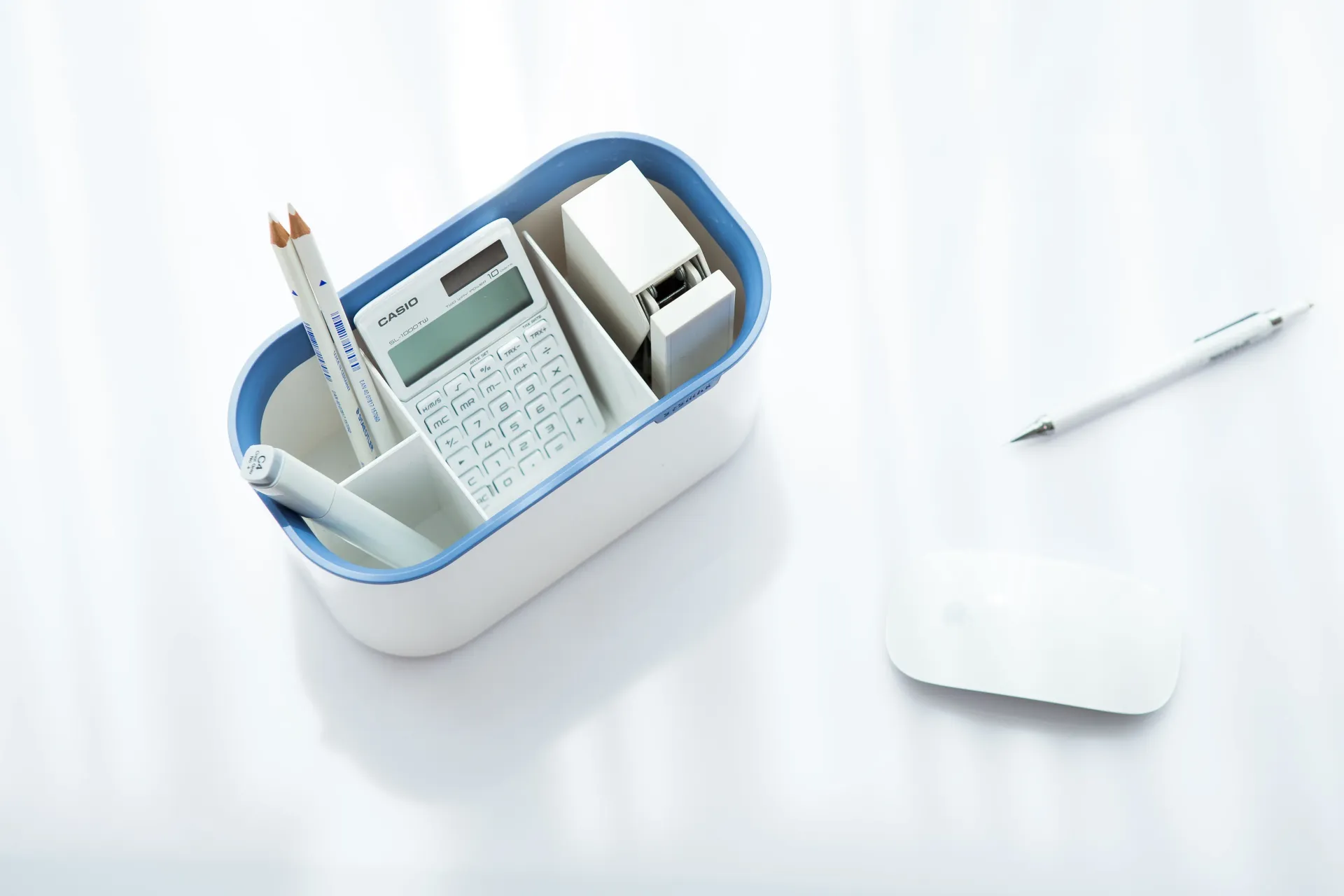 Secretaria con un bolígrafo, un ratón de ordenador y un organizador azul con varios objetos.