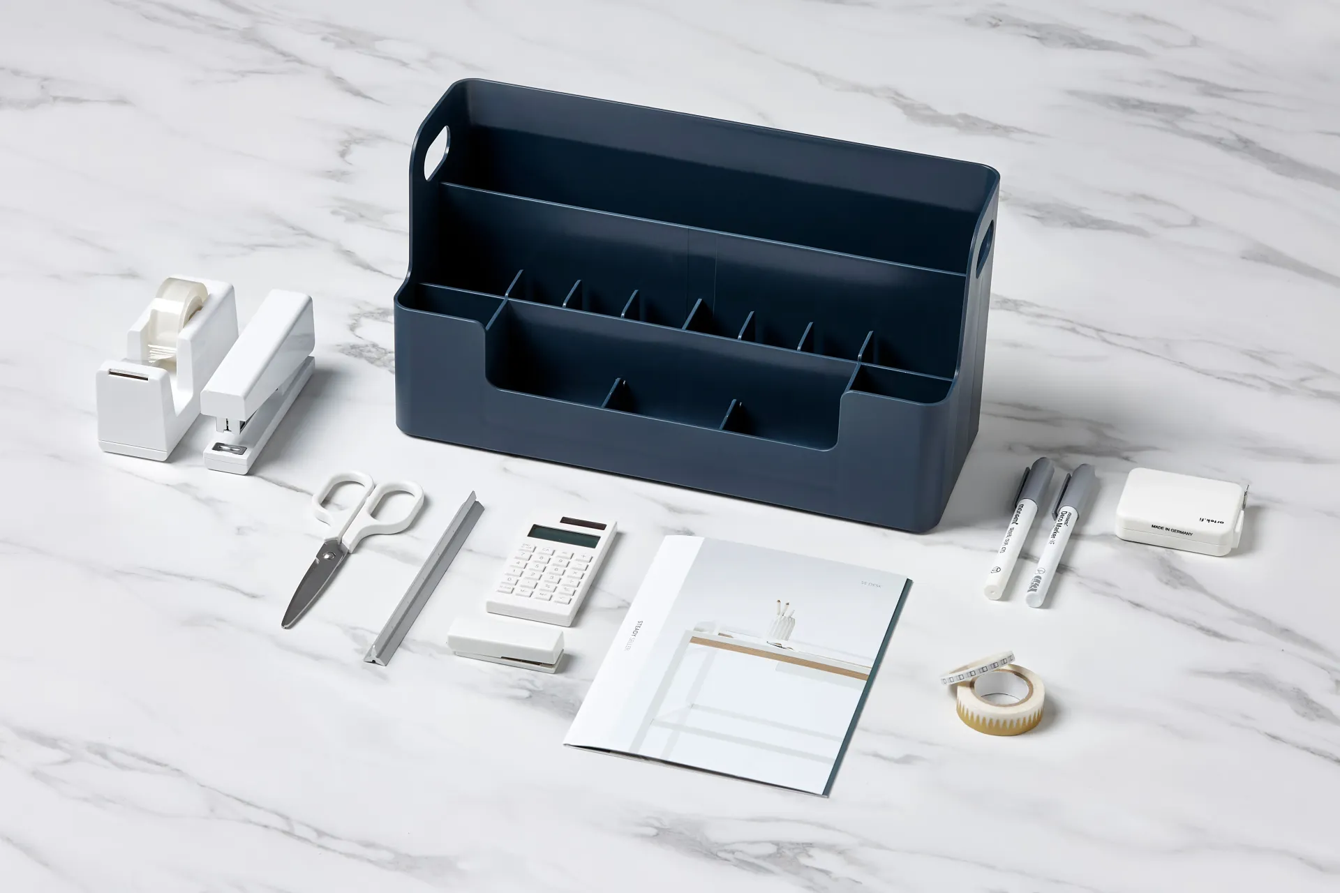 Una caja azul llena de material de oficina está sobre una mesa de mármol.