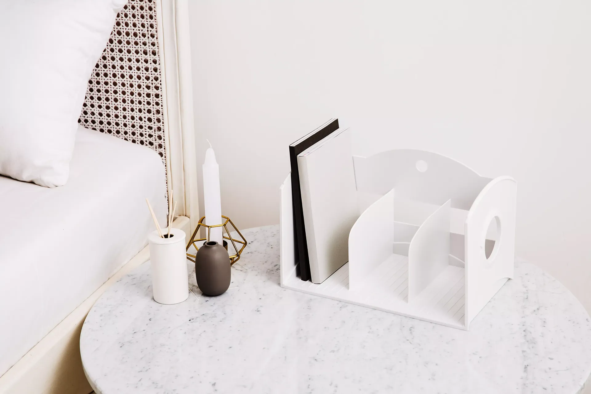 Hay un estante blanco sobre una mesa blanca junto a una cama.