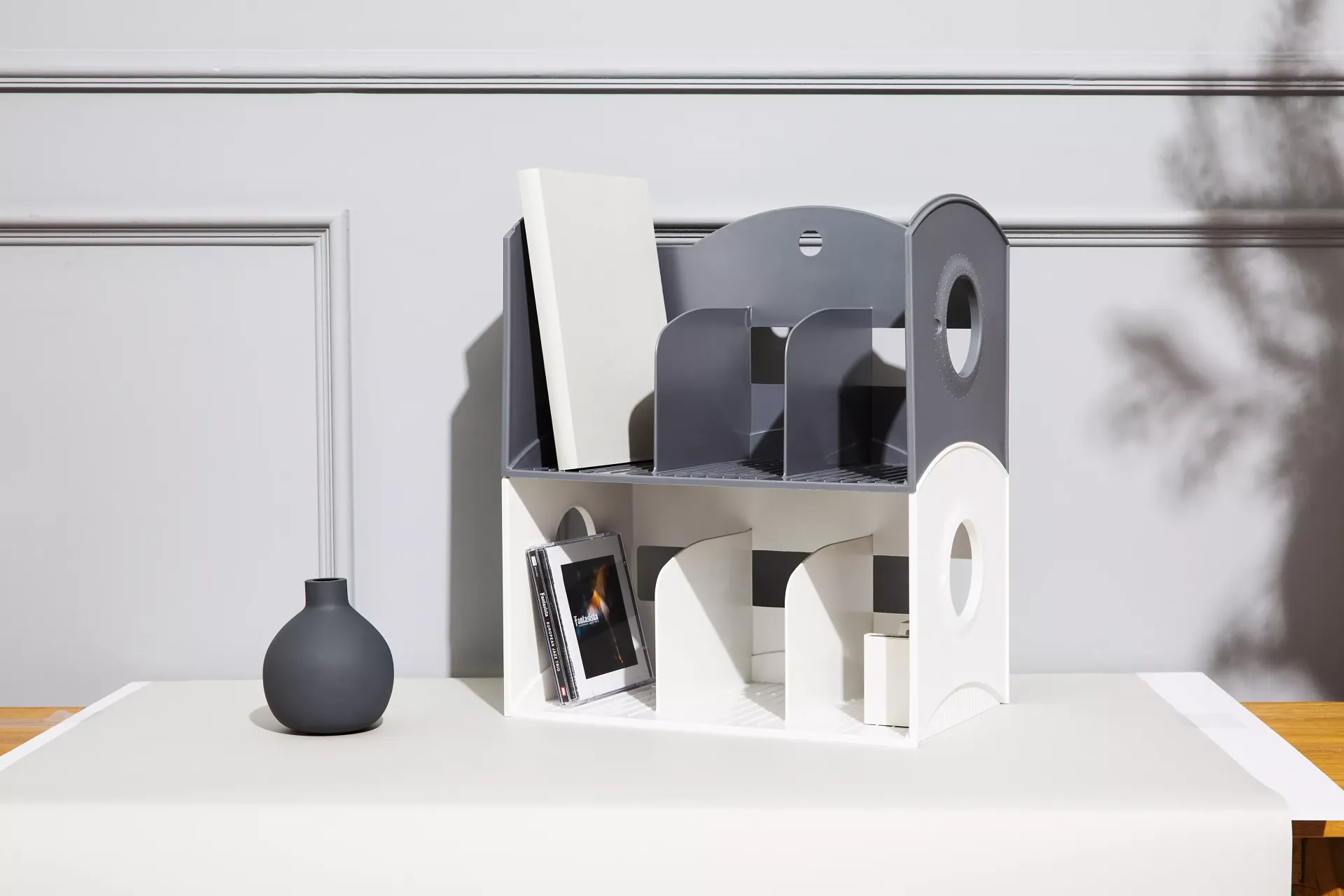 Una estantería blanca y gris está sobre una mesa junto a un jarrón.