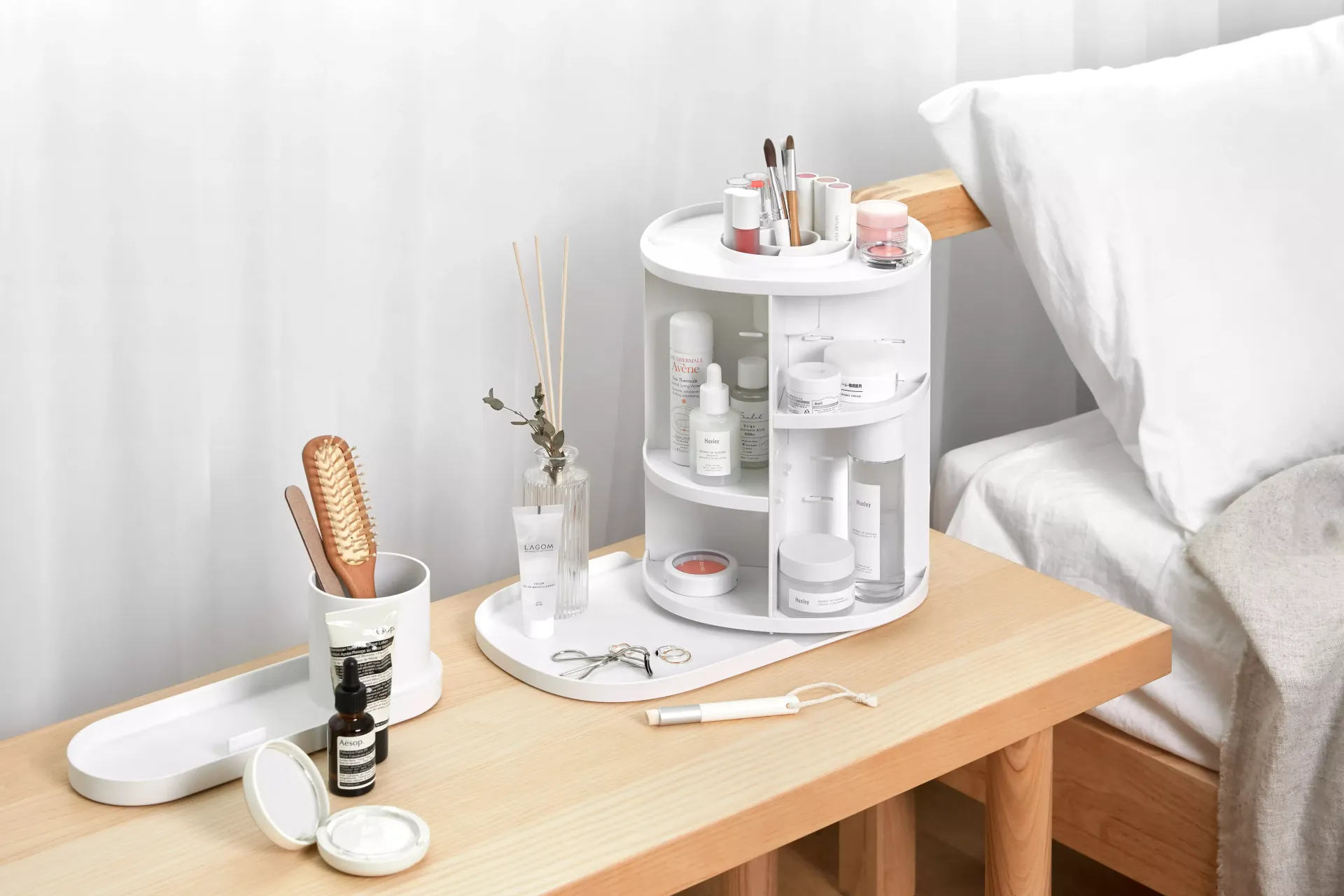 Un organizador de cosméticos blanco está sobre una mesa de madera junto a una cama.