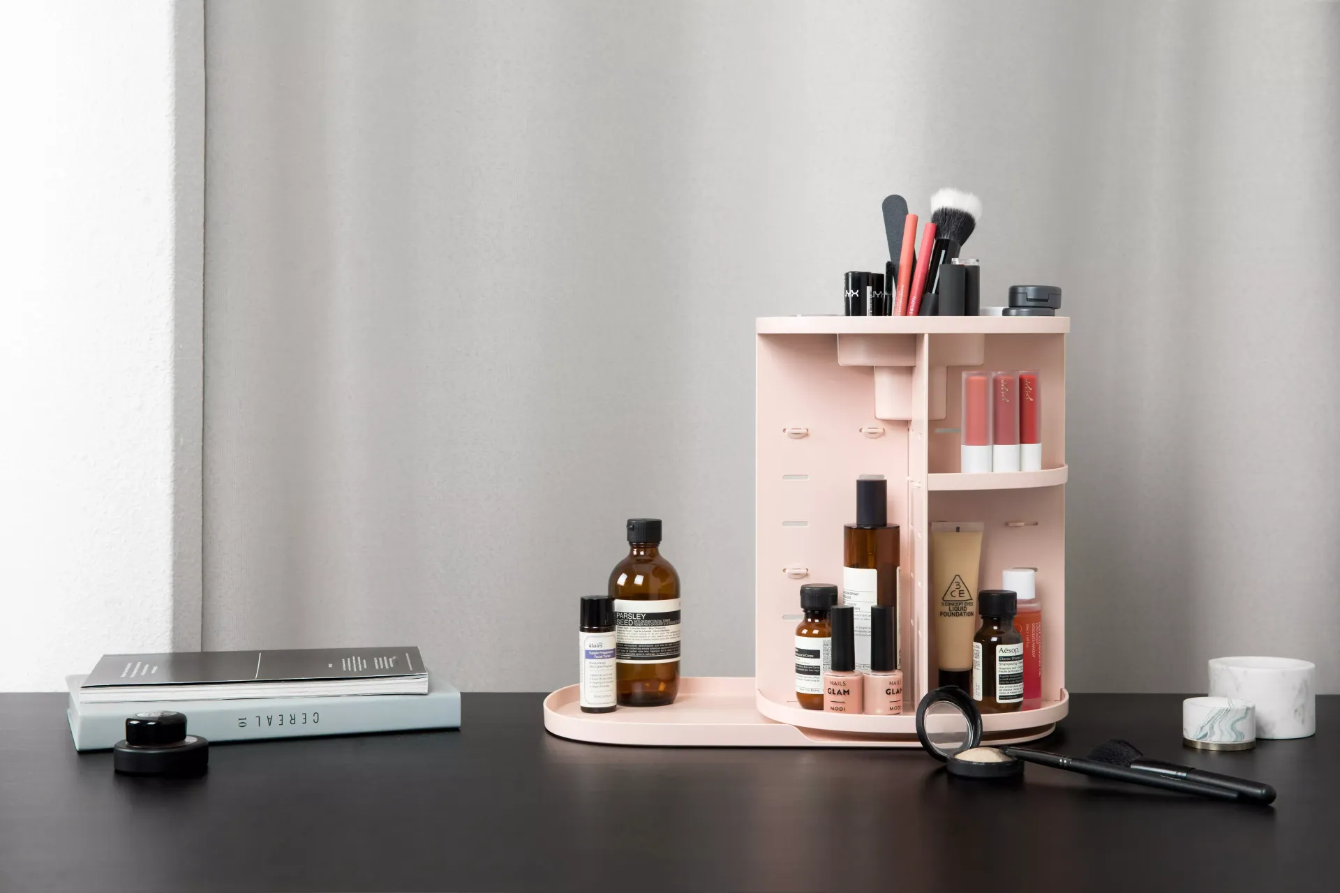 Un organizador de cosméticos rosa está sobre una mesa negra.