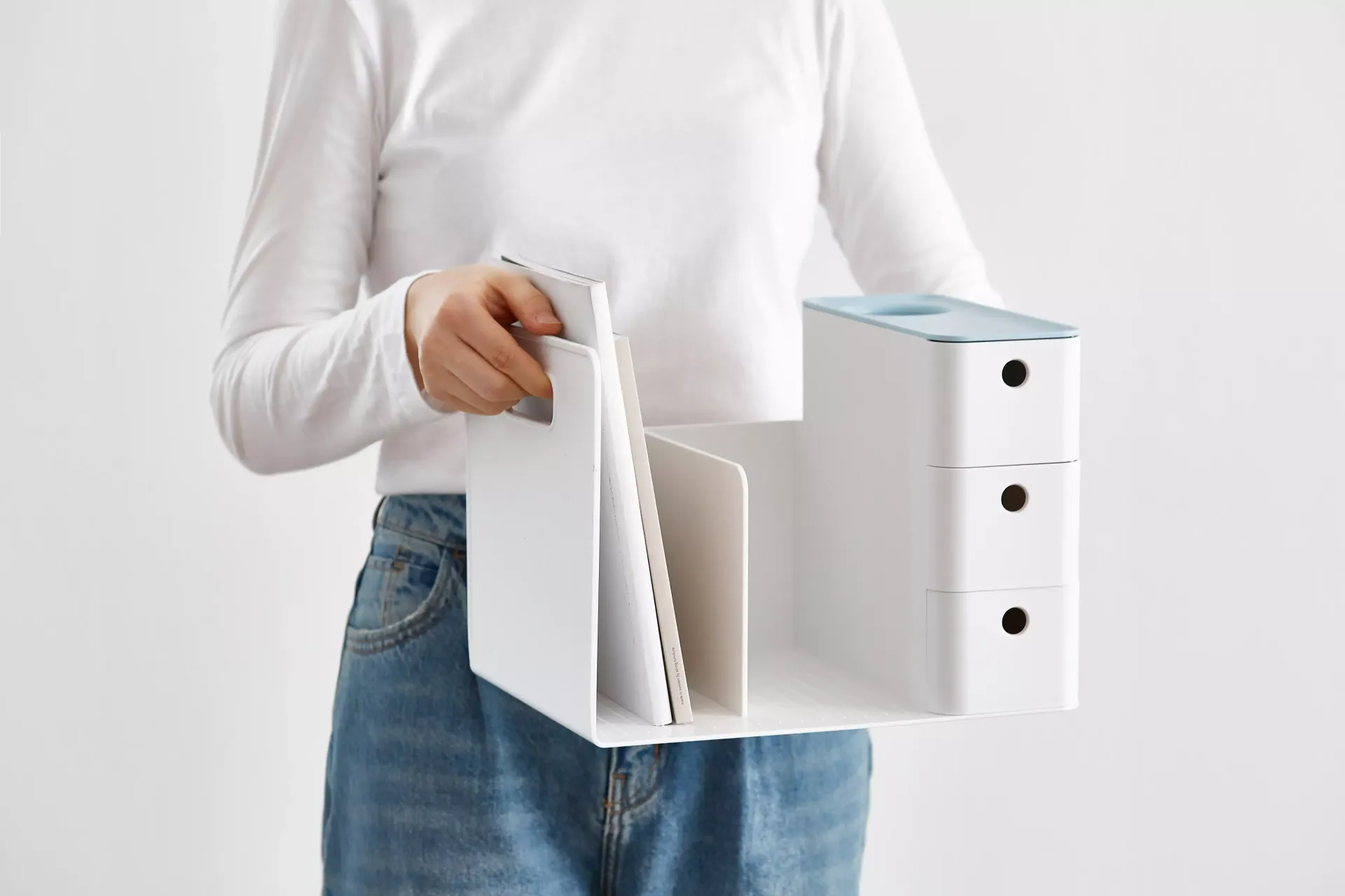 Uma mulher de camisa branca e jeans azul está segurando um organizador branco.