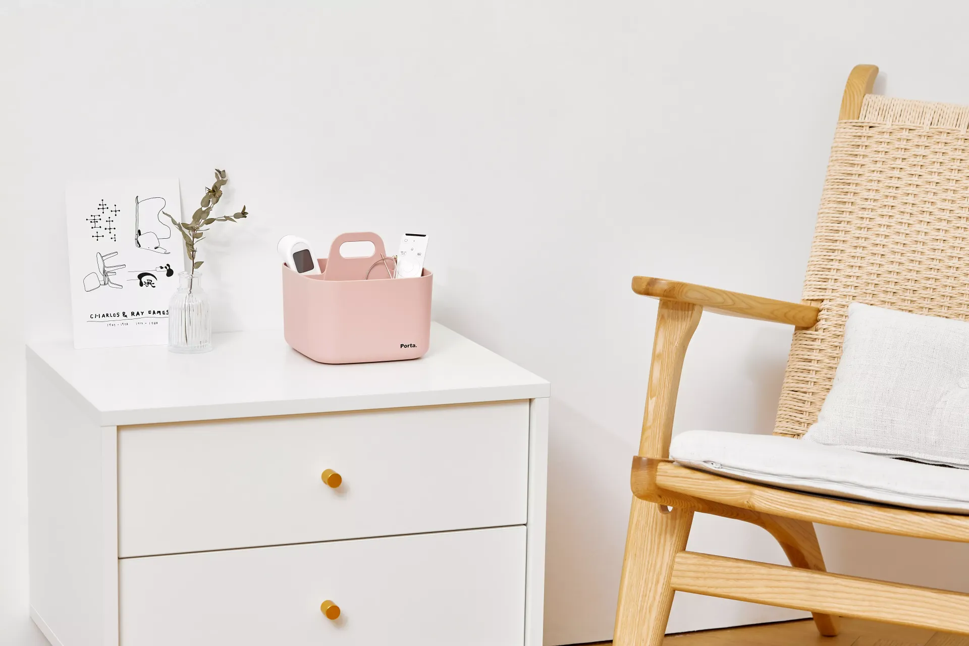 Una mecedora de madera está junto a una mesita de noche blanca con una cesta rosa encima.