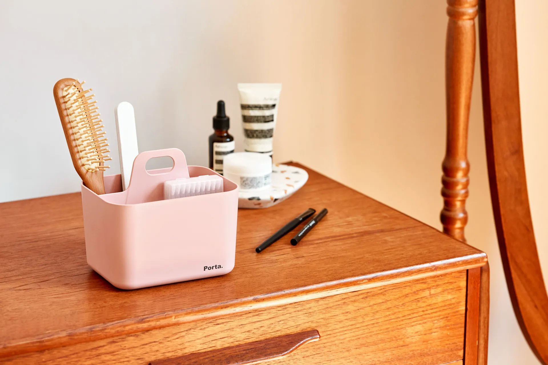 Una cómoda de madera con un recipiente rosa lleno de pinceles y cosméticos.