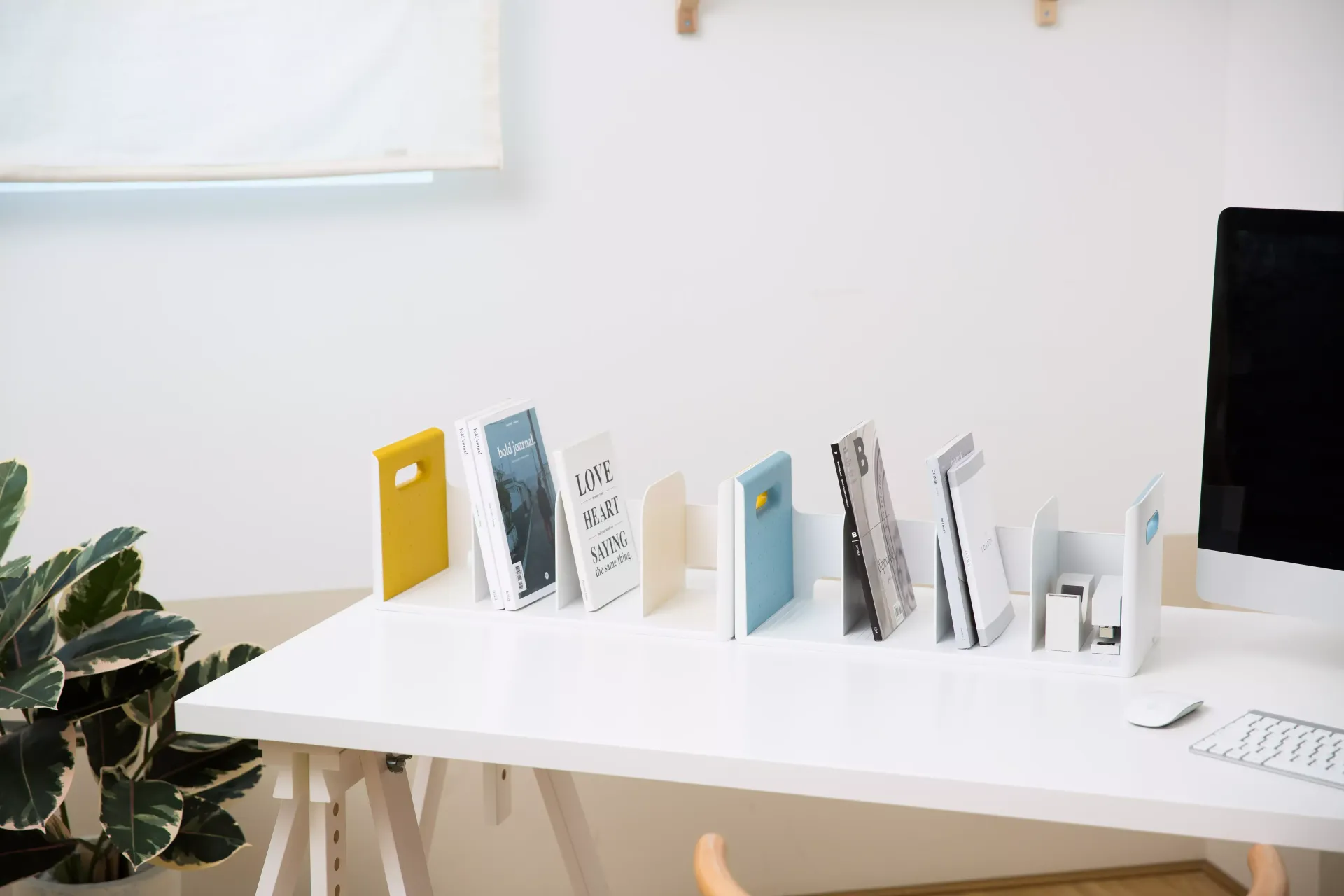 Una fila de libros sobre una mesa blanca junto a un ordenador.