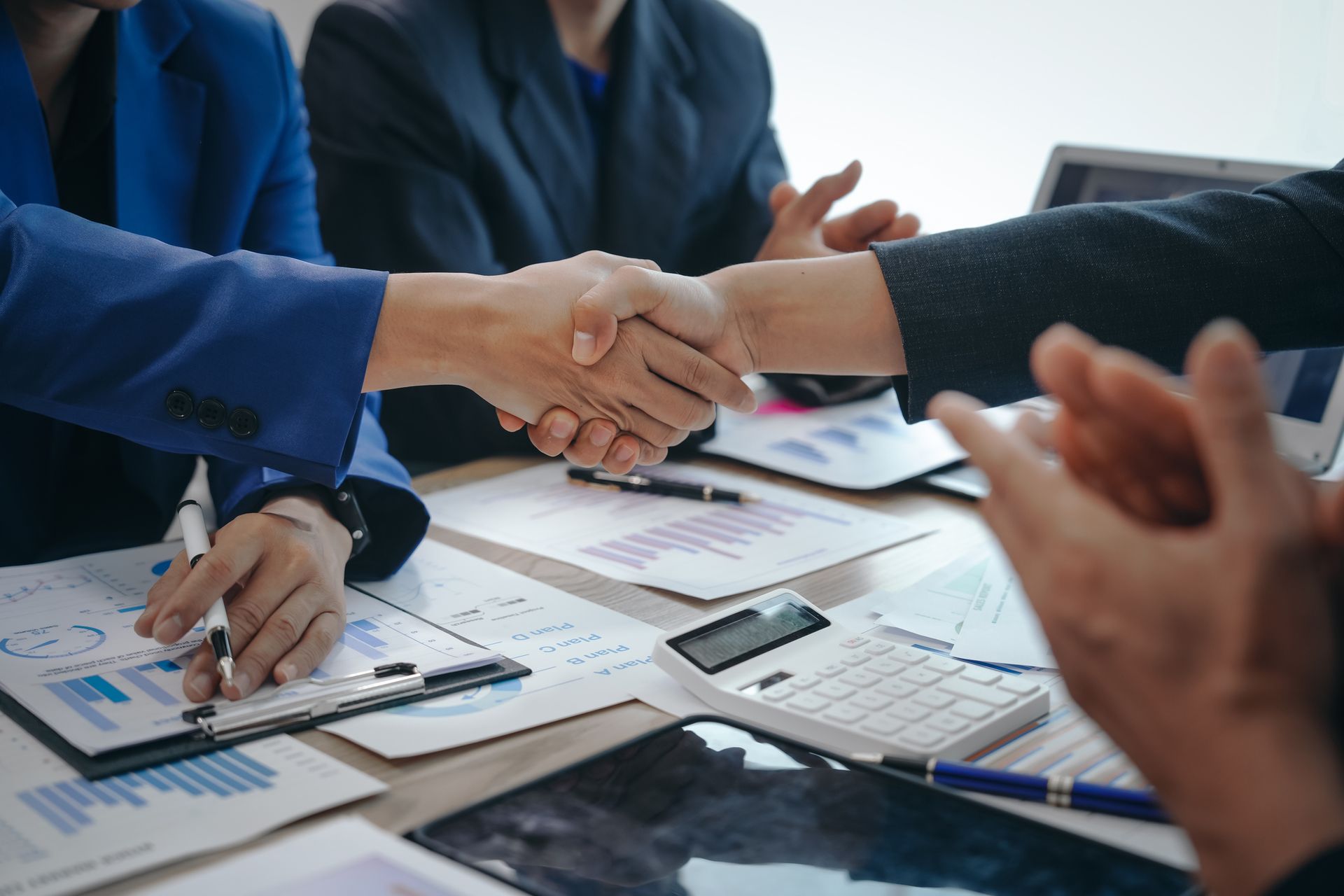 Business handshake with documents, calculator, and laptop on table. Business handshake with documents, calculator, and laptop on table.