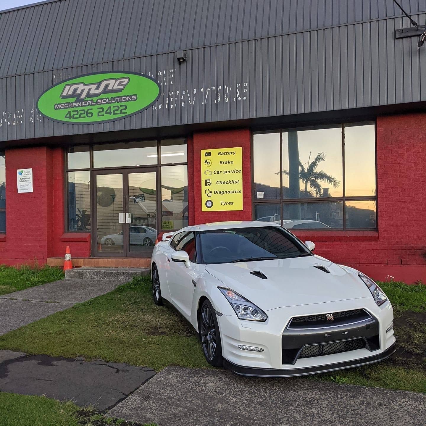 White sports car parked outside a red-and-gray storefront with a green sign and yellow window poster