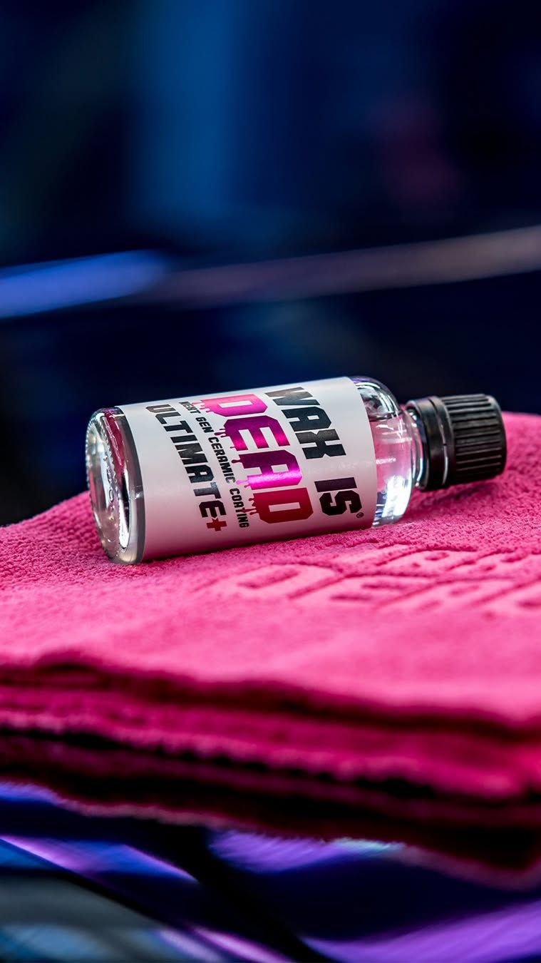 A small spray bottle on a bright pink towel, with a blurred dark background.