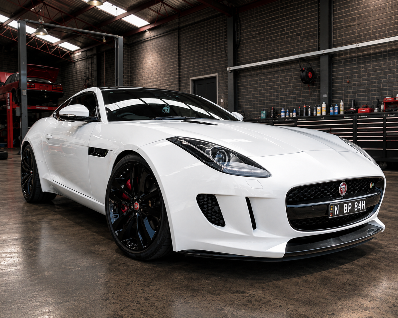 White sports car parked in an indoor garage with brick walls and glossy black wheels