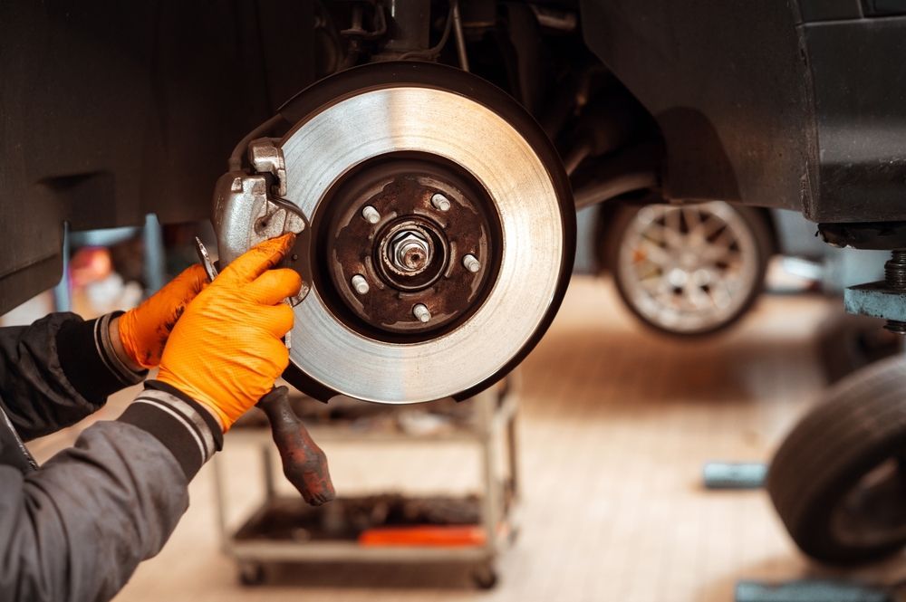 Person in a black hoodie working under a car with a tool, looking upward in a dim garage.